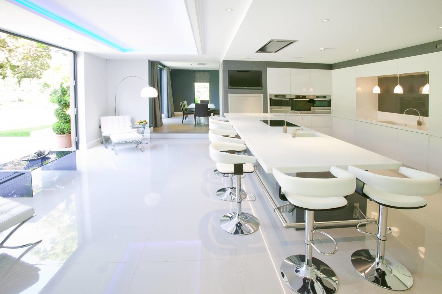 a kitchen with a long counter and white chairs.