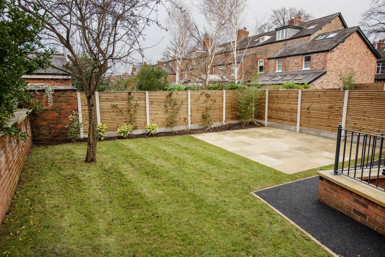 a backyard with a fence, grass and a tree.