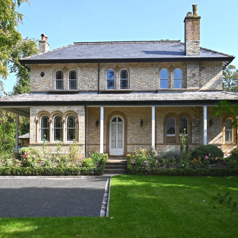 A grandiose stone house with a driveway and trees undergoing renovation.
