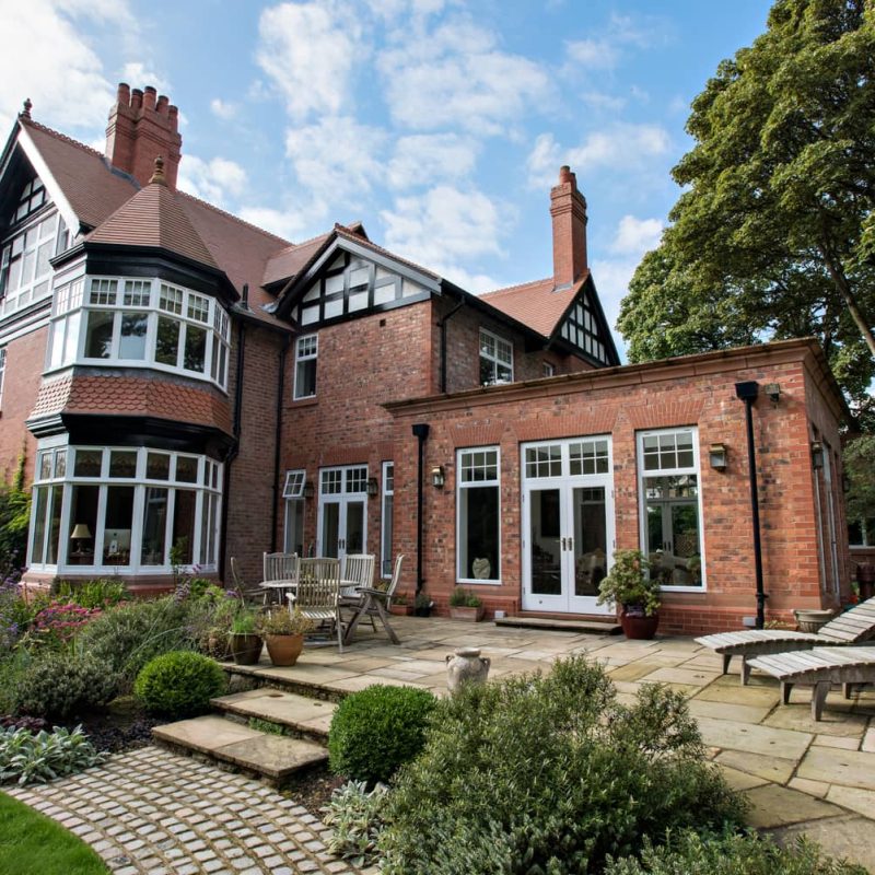 A large red brick house with a lawn and patio, undergoing restoration.